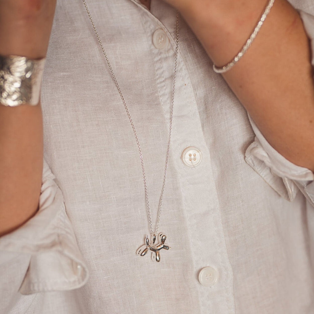 Sterling Silver Supersize Balloon Dog Necklace on a long chain and worn on a model over a white shirt.