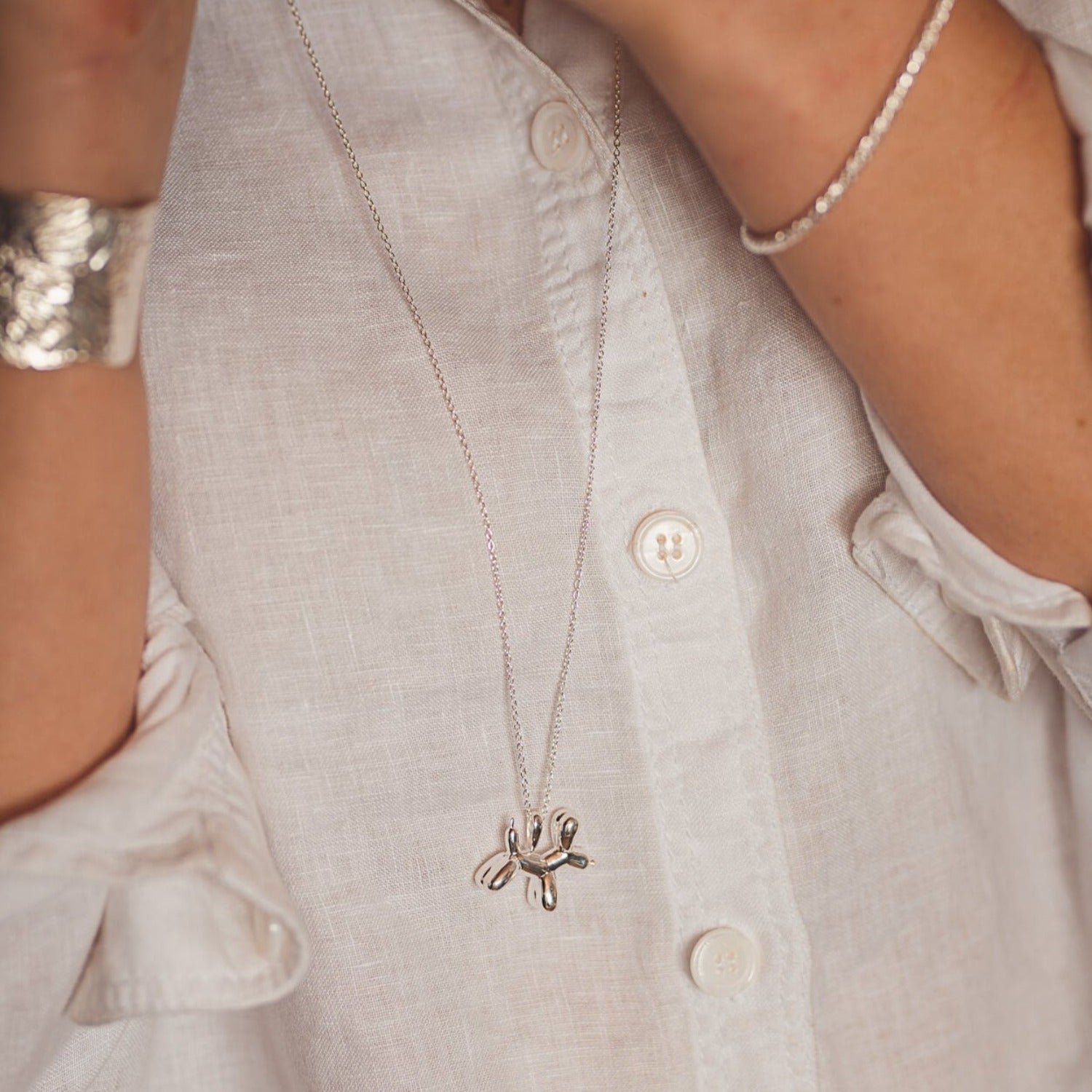 Sterling Silver Supersize Balloon Dog Necklace on a long chain and worn on a model over a white shirt.