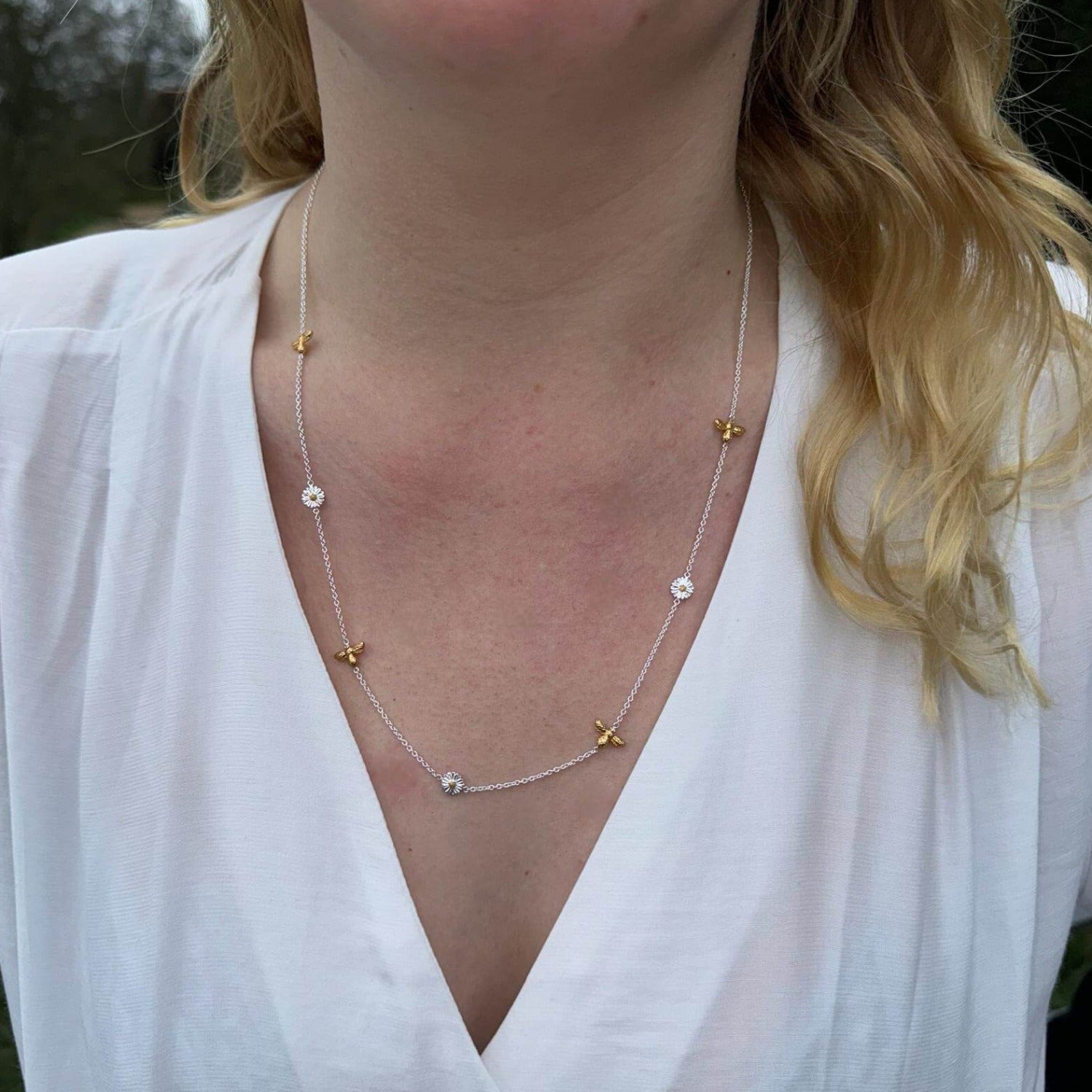 A Sterling silver chain necklace, with silver bumble bees, gold plated bumble bees and daisies spread evenly along the fine chain. Worn on a models neck wearing a white blouse.