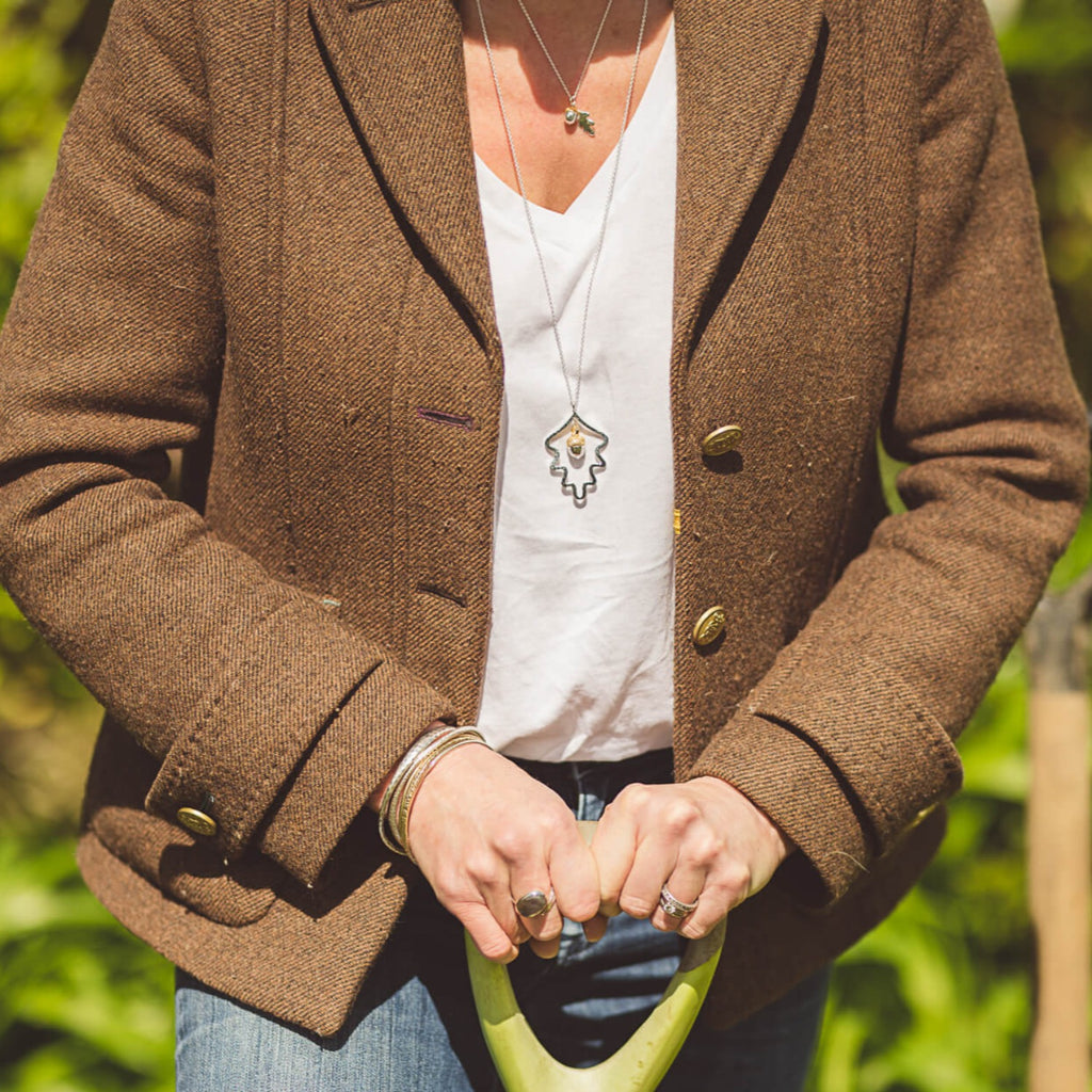 A sterling silver oak leaf silhouette with an acorn hanging inside the leaf. The design hangs from a long chain, worn on a lady doing gardening.