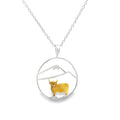 A sterling silver circular pendant with an 18ct gold plated highland cow with silver hills inside the circle. The pendant hangs from a sterling silver adjustable chain.