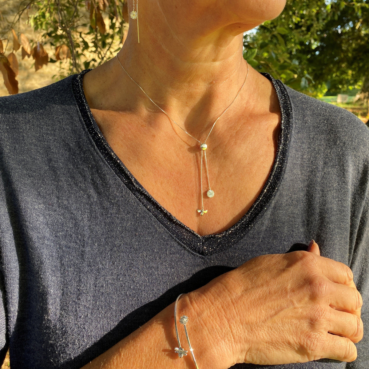 A daisy and bee necklace and cuff bracelet being worn on a model in the sushine