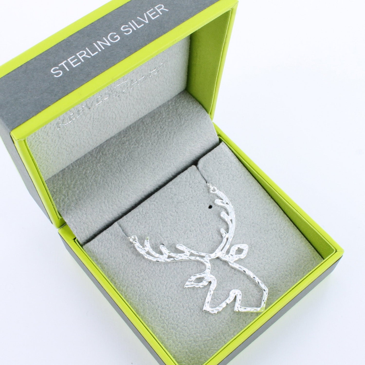 A silver stag head silhouette necklace with a hammered finish. Hung on a silver chain and shown in a Reeves & Reeves grey and green gift box.