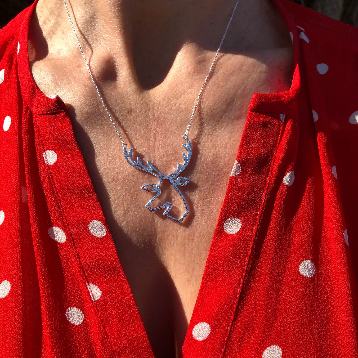 A close-up of a person wearing a silver stag head necklace in a silhouette style styled with a red and white polka dot blouse.