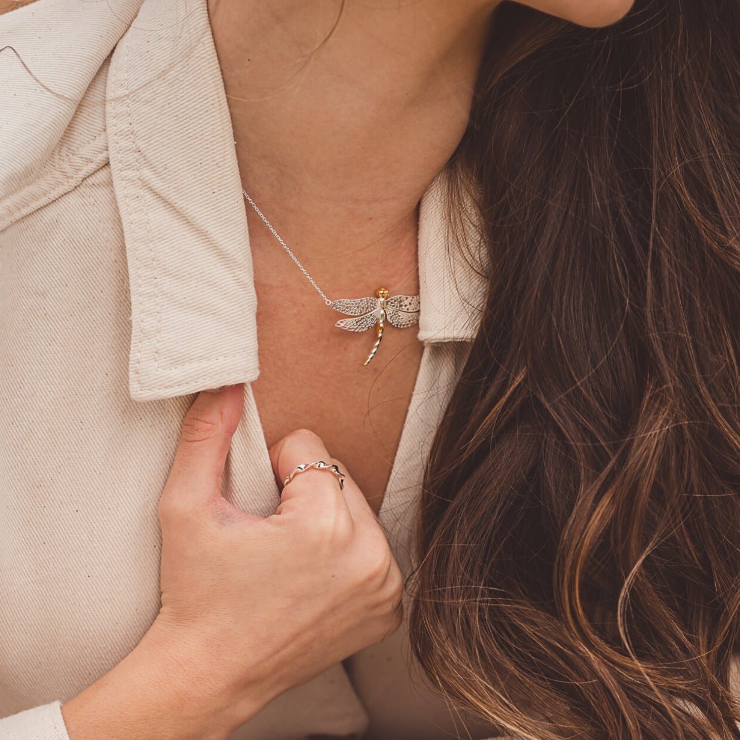 A Sterling Silver Dragonfly Necklace with 18ct yellow and rose gold plate detail on its body, hanging from a silver chain and worn on a models neck.