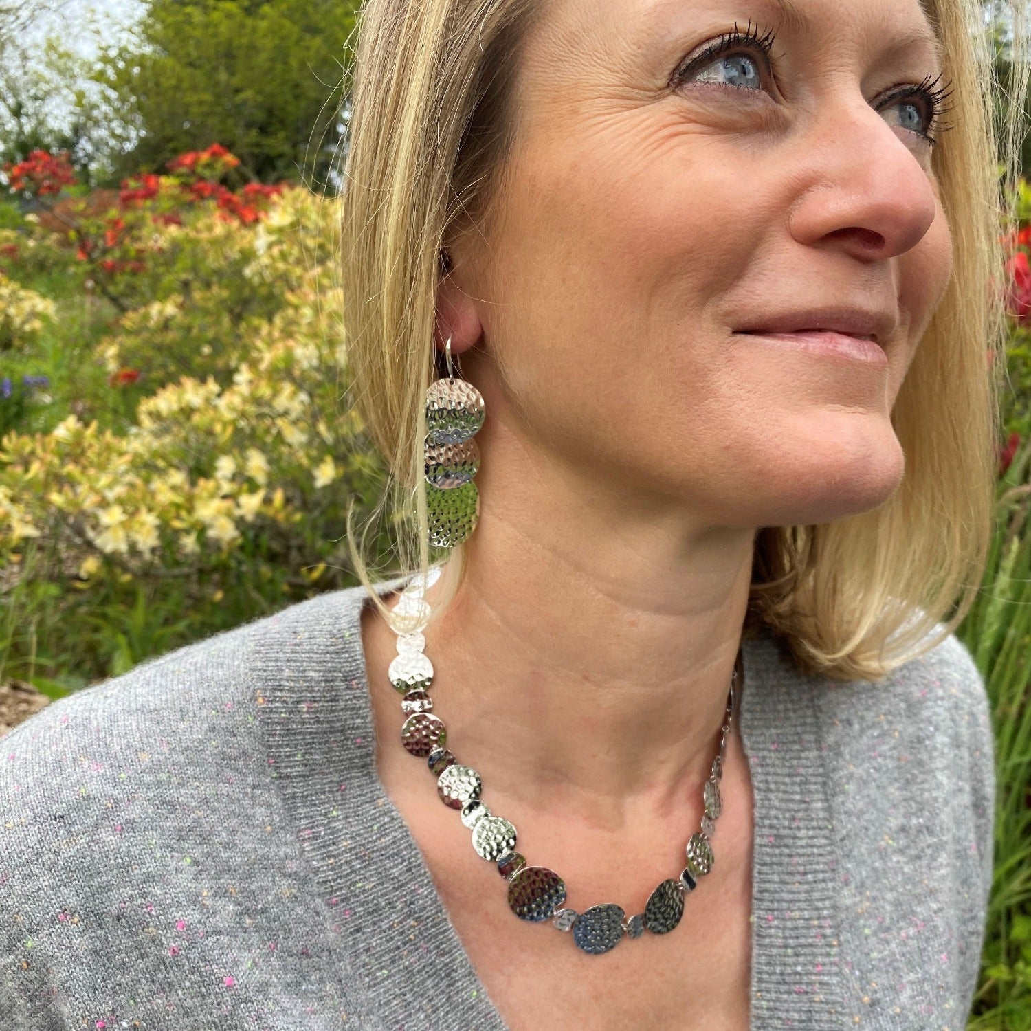 A sterling silver necklace comprising of circular shapes that have a hammered finish, worn on a model with the matching earrings.