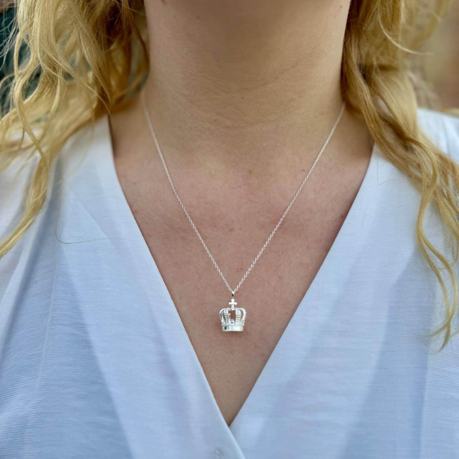 A sterling silver Regal Crown Necklace with intricate details, hanging on a silver adjustable chain and worn on a ladies neck.