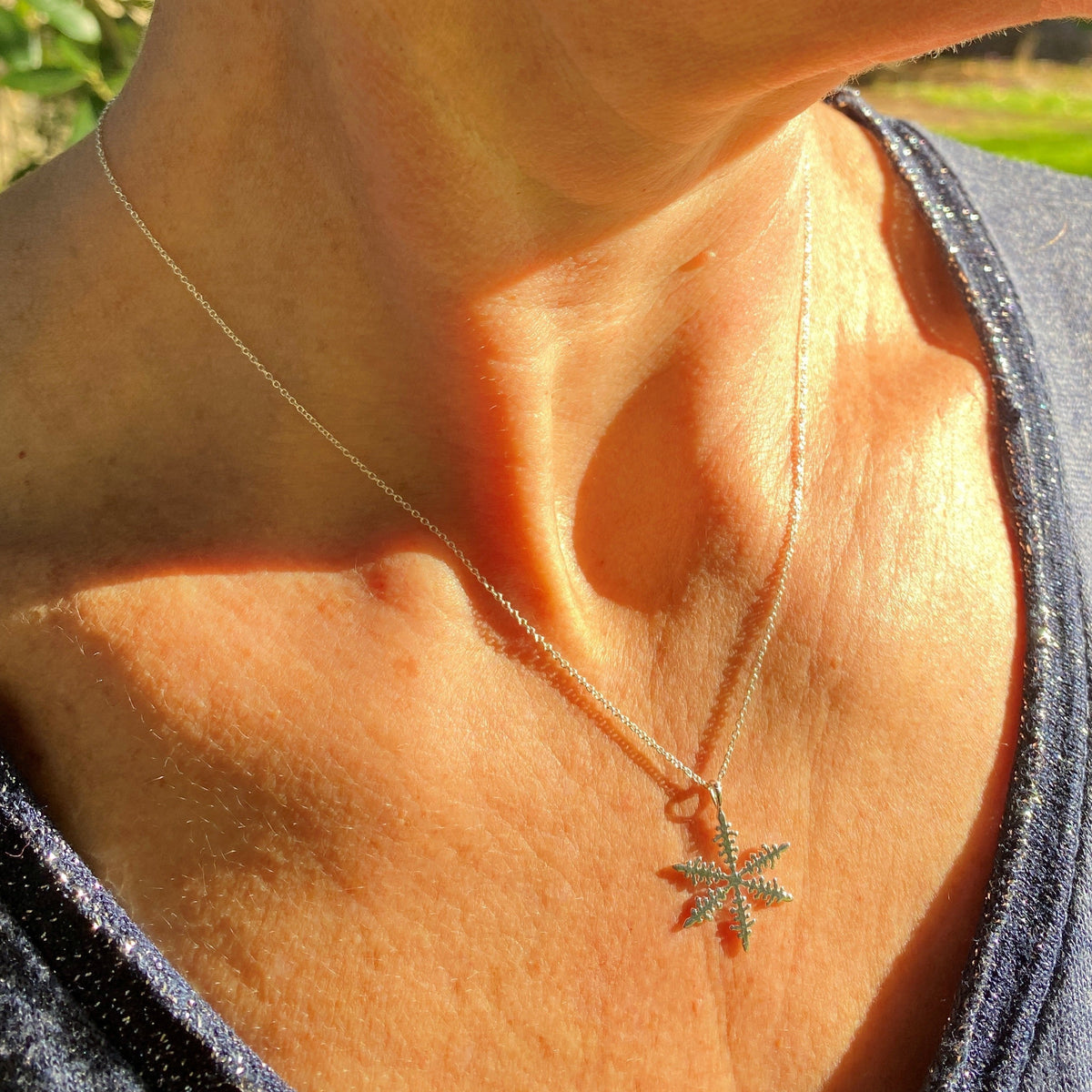 A silver snowflake necklace being worn on a neck
