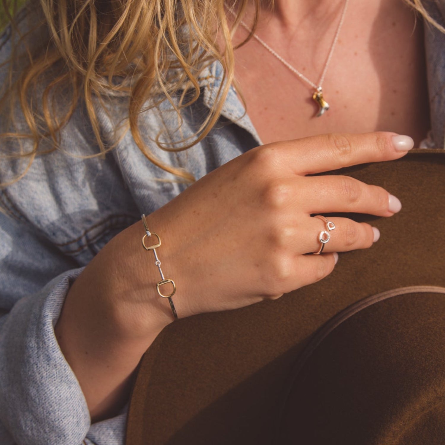 A silver and gold plated snaffle cuff bracelet worn on a model who is wearing other equestrian themed jewellery.
