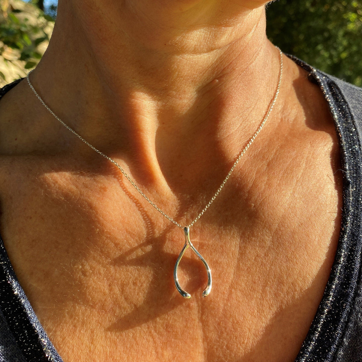 A solid silver wishbone pendant sparkling in the sunshine and worn on a very attractive model