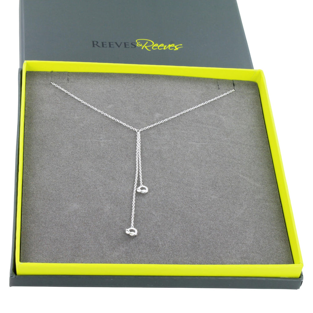 A silver Y-shaped dangle necklace with small knot charms, presented in an open Reeves & Reeves gift box.