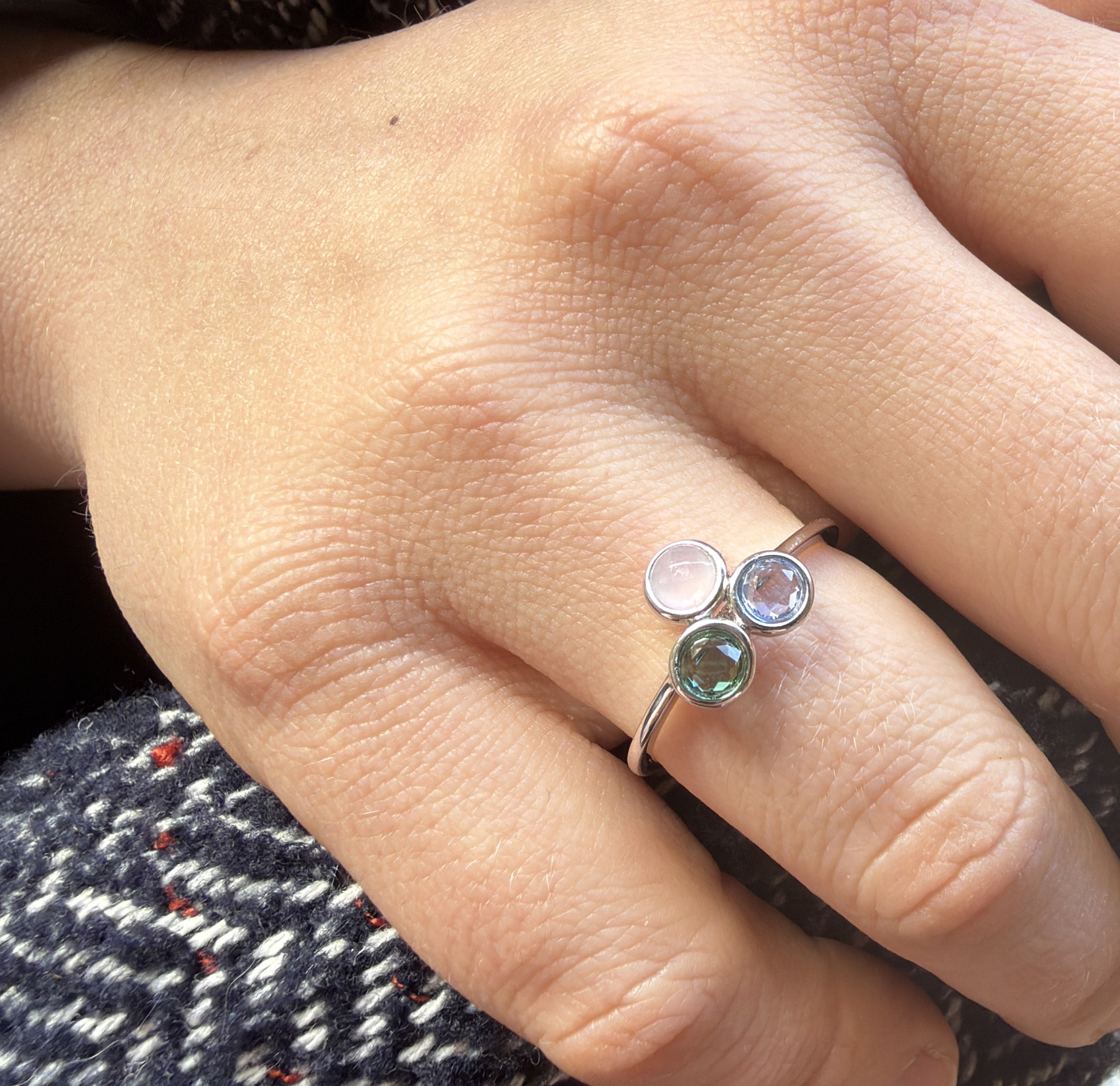 Close-up of a hand wearing a silver ring with three gemstones.