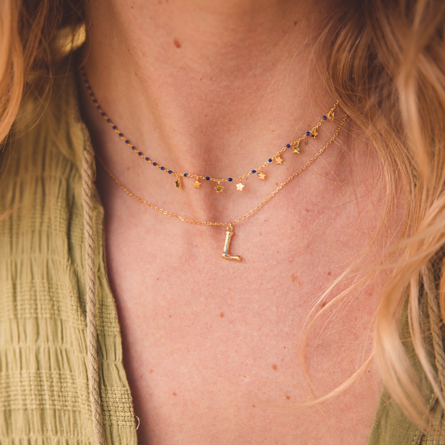 Sterling Silver and gold plated star charm necklace. The chain is set with navy blue enamel beads spread evenly, and nine gold plated star charms hang along the front of the chain. Worn on a model, layered with an 'L' initial necklace.