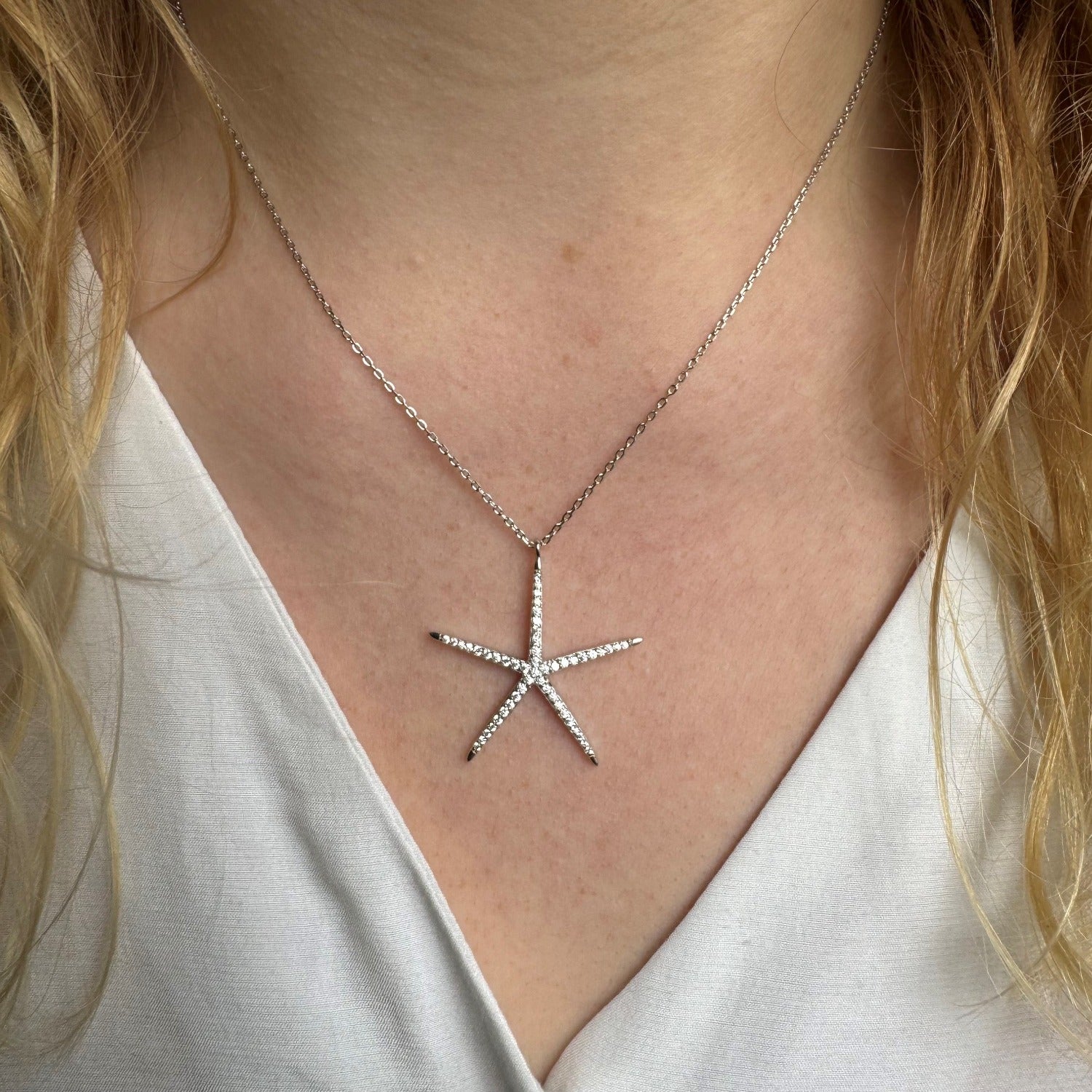 A Sterling Silver Large Starfish Necklace, filled with cubic zirconia stones and hanging on a silver chain. Worn on a models neck.