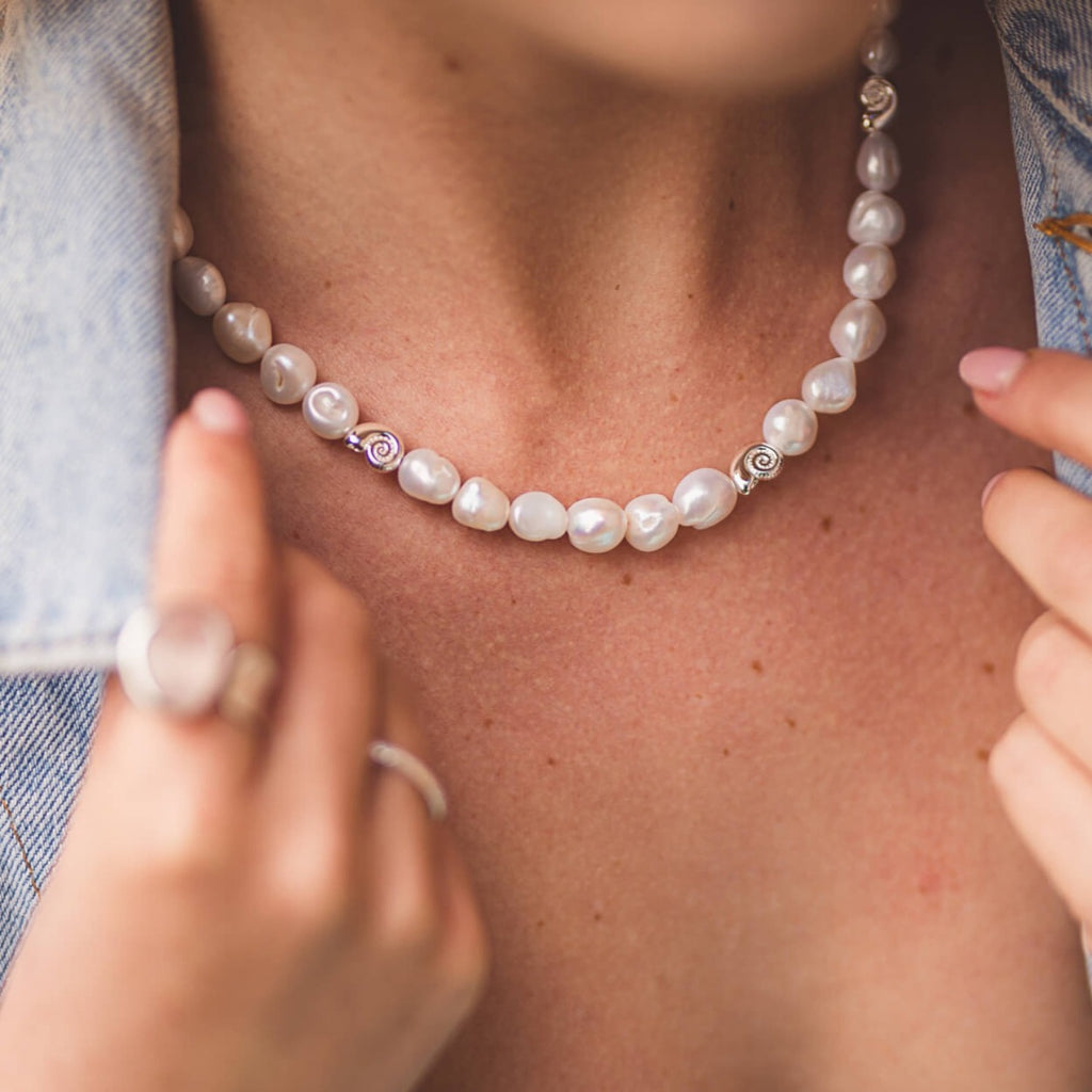 A sterling silver necklace with white freshwater pearls all along the chain. The pearls are interspersed with silver ammonites. Worn on a models neck.
