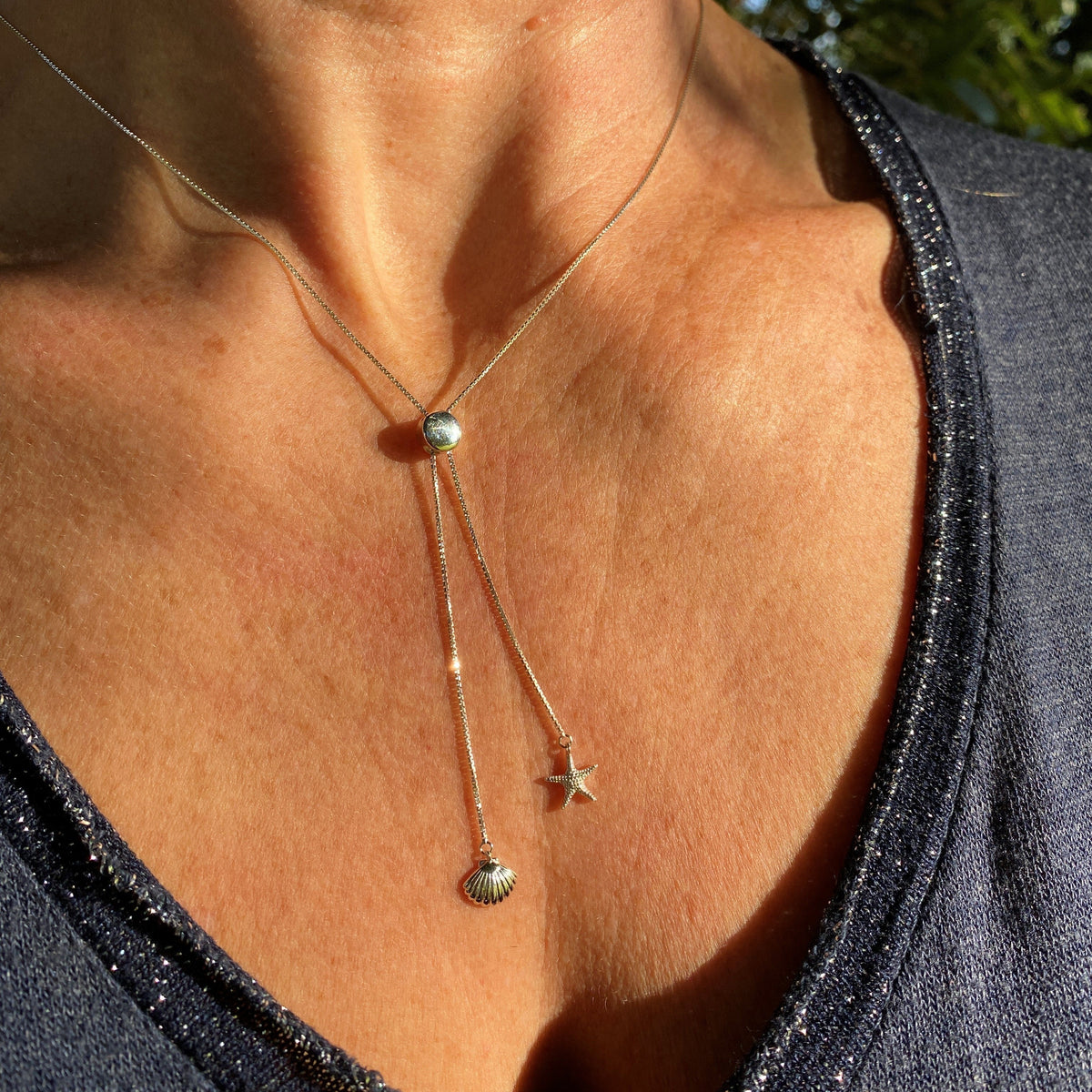 A silver necklace with a starfish and shell detail being wortn on a very attractive model