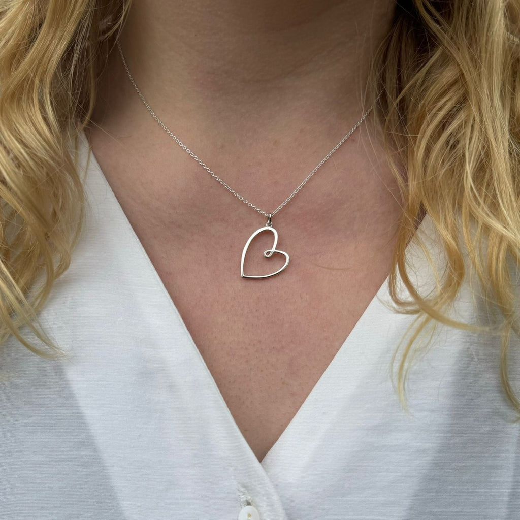 A silver heart pendant, hanging on an adjustable silver chain, worn on a ladies neck.