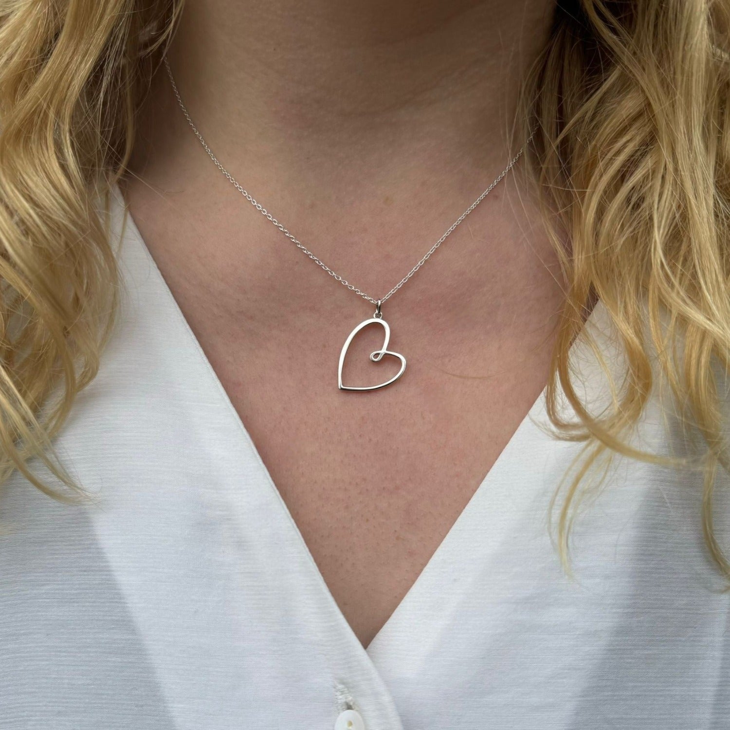 A silver heart pendant, hanging on an adjustable silver chain, worn on a ladies neck.