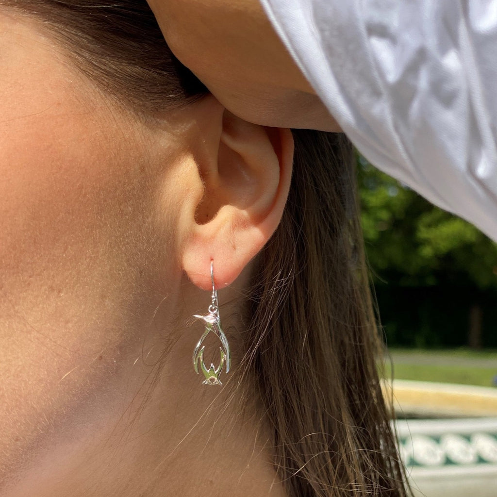A sterling silver penguin silhouette drop earring, hanging on a silver hook and worn in a ladies ear.