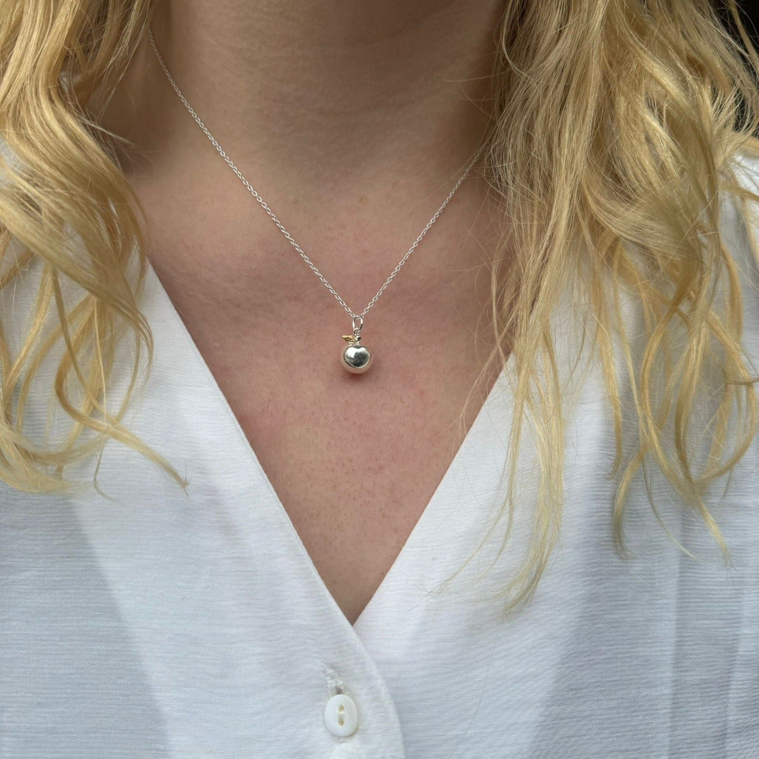 A silver apple pendant with a gold plated leaf detail, hanging on a silver chain and worn on a model.