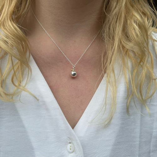A silver apple pendant with a gold plated leaf detail, hanging on a silver chain and worn on a model.