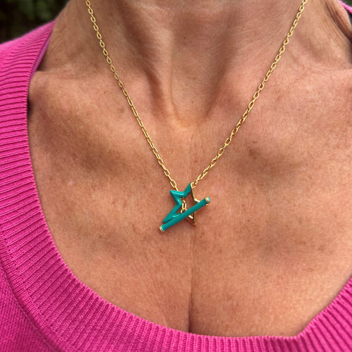 A gold plated star silhouette, half covered in turquoise enamel with a turquoise enamel t bar through the centre, hung on a gold chain and worn on a models neck.