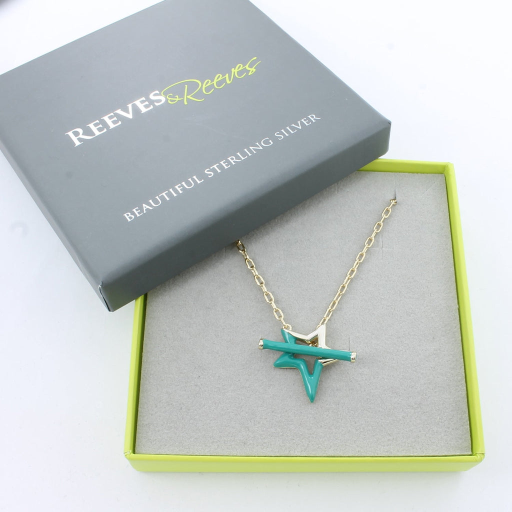 A gold plated star silhouette necklace, half the star is dipped in turquoise enamel detail with a turquoise t bar through the centre. Shown in a Reeves & Reeves grey and green gift box.