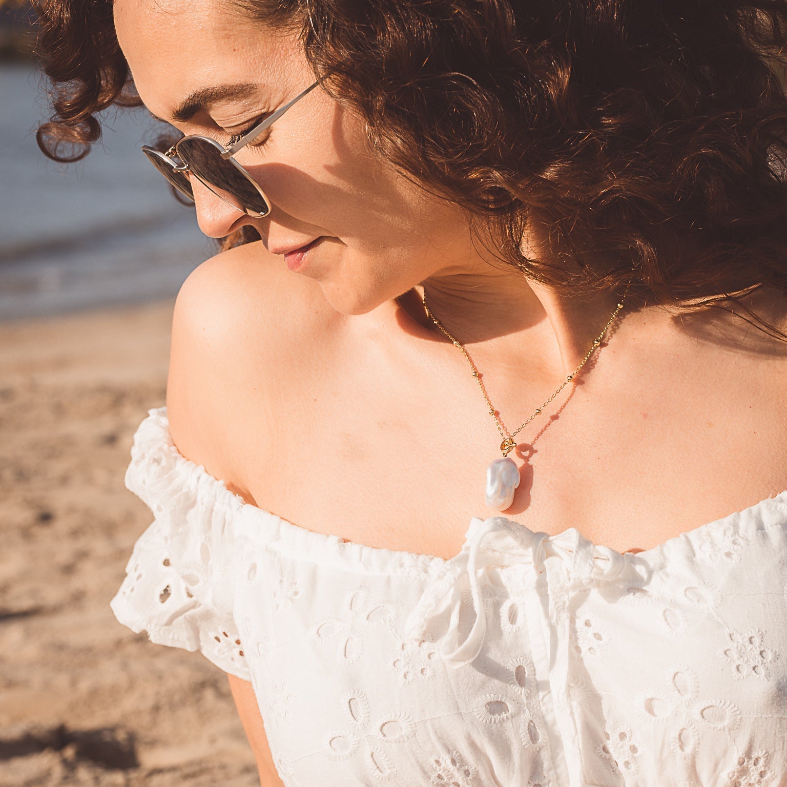 A sterling silver and gold plated beaded chain with a baroque white pearl sat as the central feature. The necklace is worn on a model at the beach.