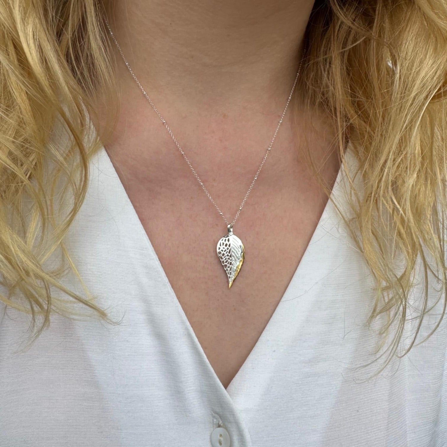 A sterling silver beech leaf necklace with a gold plated edge, hanging on a fine silver chain and worn on a models neck.