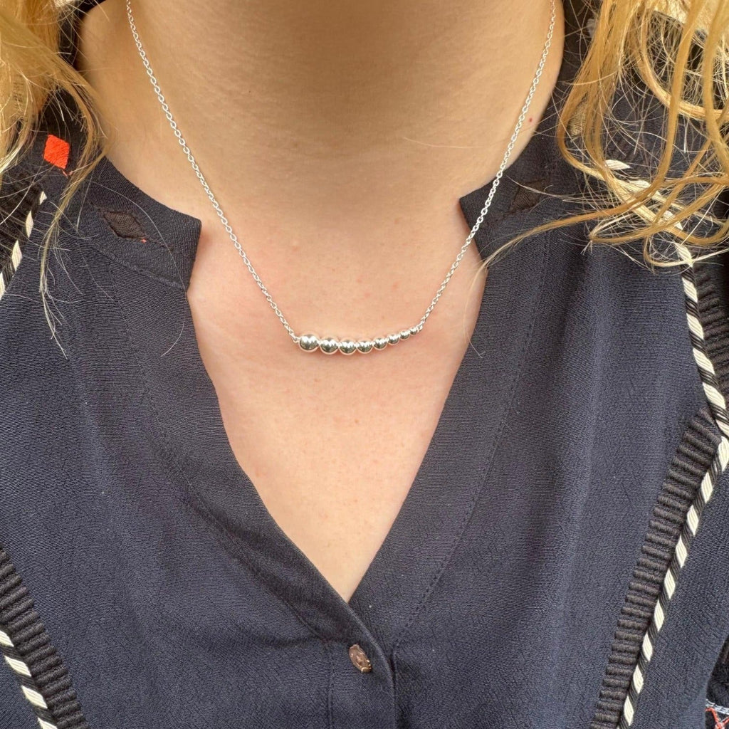 A sterling silver necklace with high shine beads in a decreasing size from left to right, hung centrally on a silver chain and worn on a model.