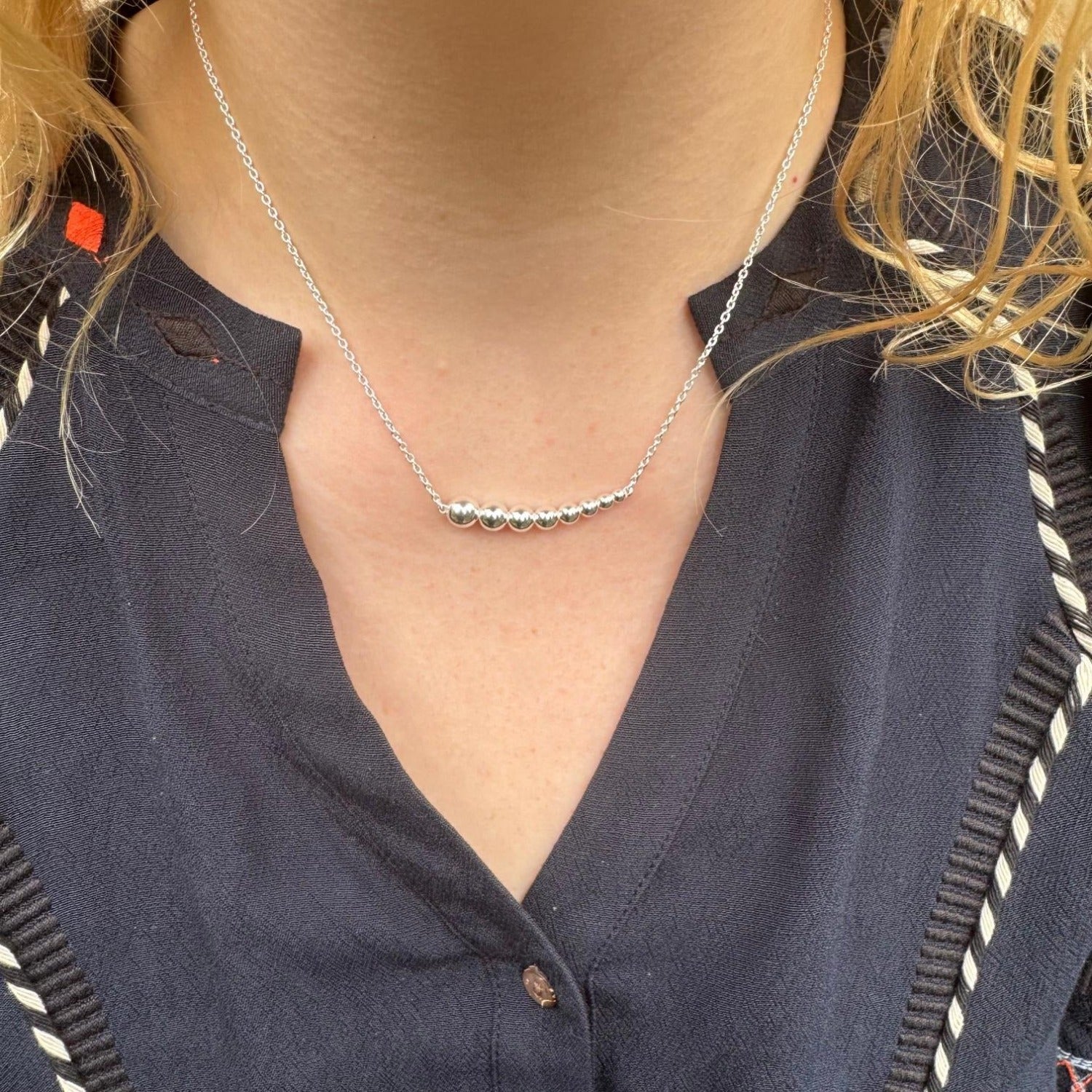 A sterling silver necklace with high shine beads in a decreasing size from left to right, hung centrally on a silver chain and worn on a model.