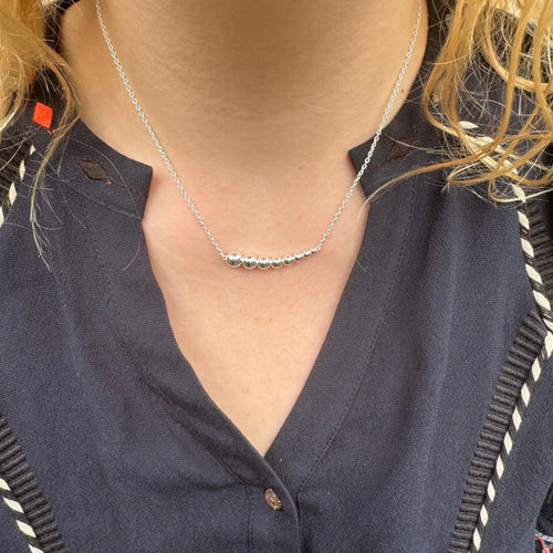 A sterling silver necklace with high shine beads in a decreasing size from left to right, hung centrally on a silver chain and worn on a model.
