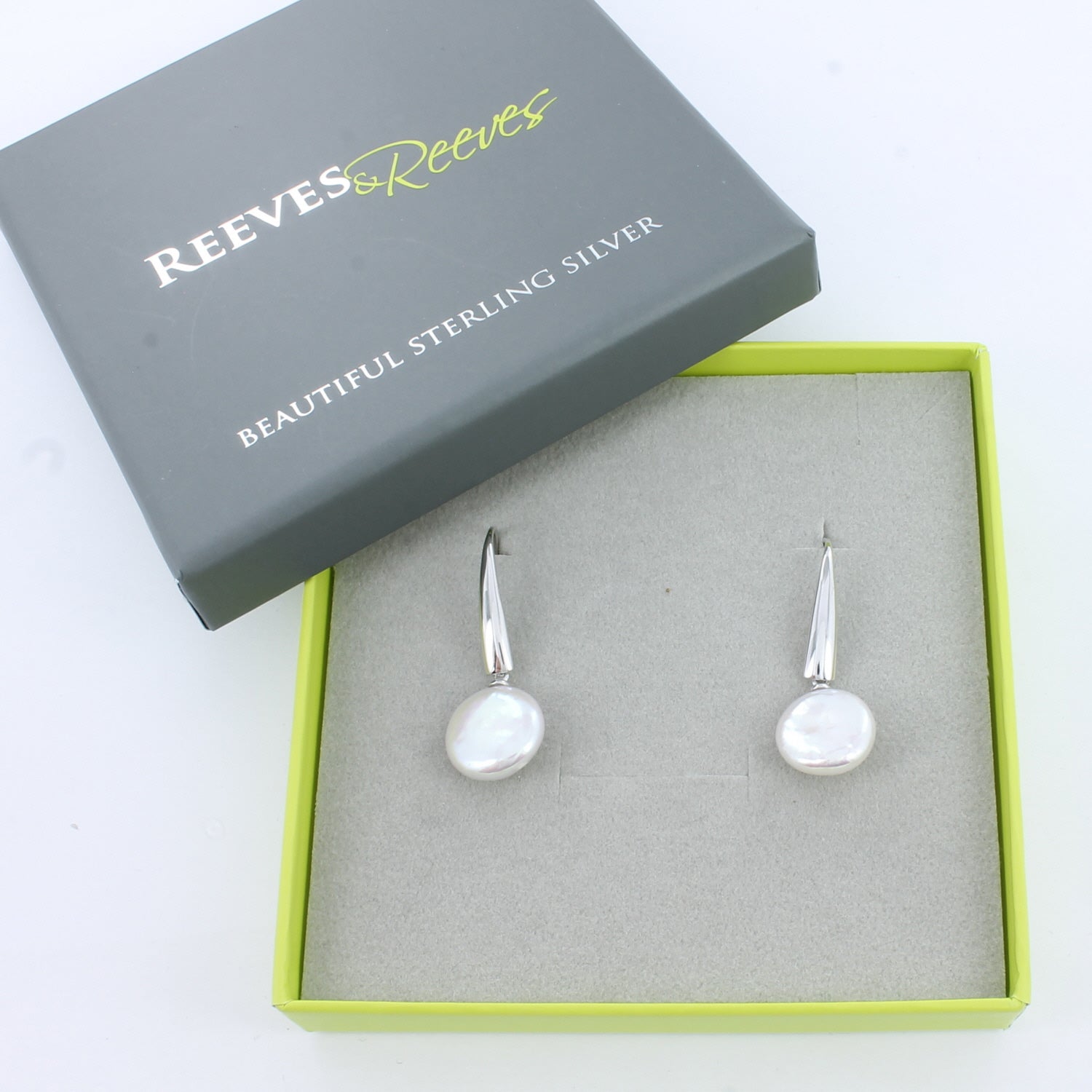 Sterling Silver hook style earrings with white button pearls hanging from the hooks. Shown in a Reeves & Reeves grey and green branded gift box.