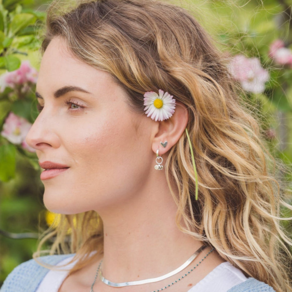 A lady wearing a pair of sterling silver heart stud earrings in her ear.