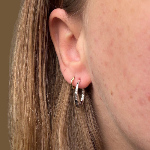 A silver pair of hammered hoops worn in a ladies ear with a smaller gold hoop worn in the second piercing.