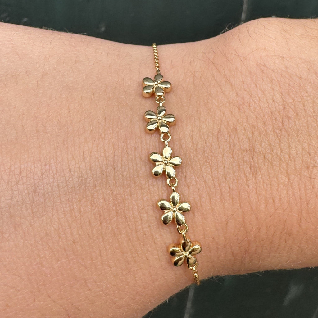 Gold plated daisy chain bracelet, worn on on a wrist against a neutral background.