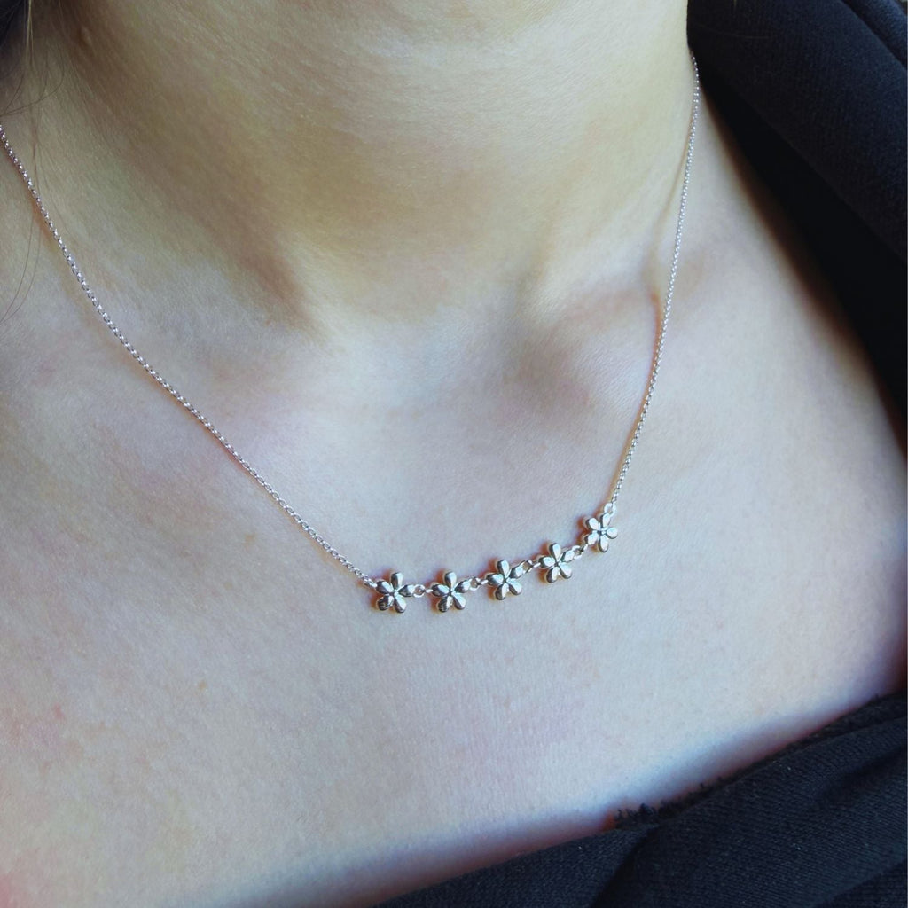 Necklace with five adjoining flowers in a chain across the centre of the fine silver chain. Worn on a person's neck.