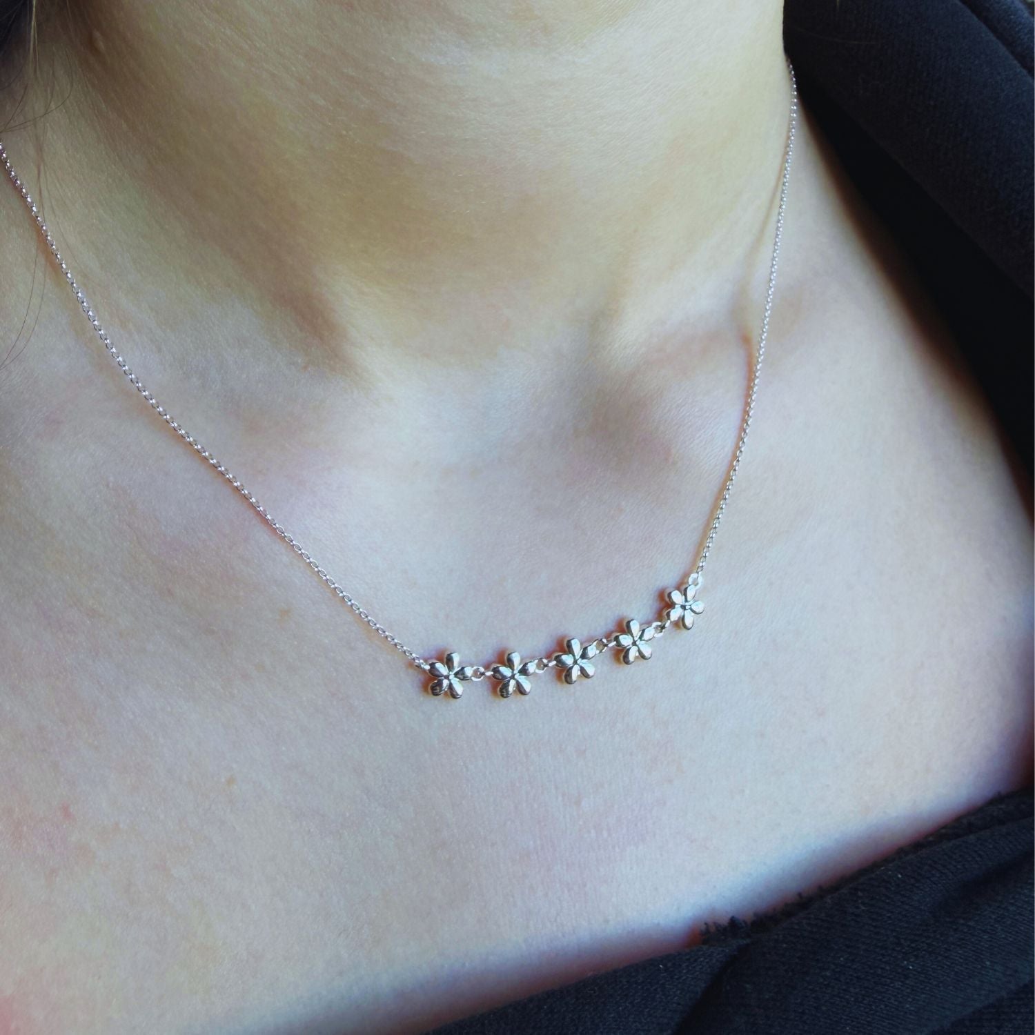 Necklace with five adjoining flowers in a chain across the centre of the fine silver chain. Worn on a person's neck.