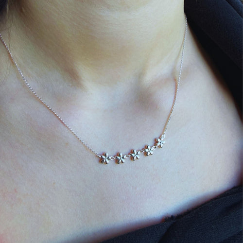 Necklace with five adjoining flowers in a chain across the centre of the fine silver chain. Worn on a person's neck.