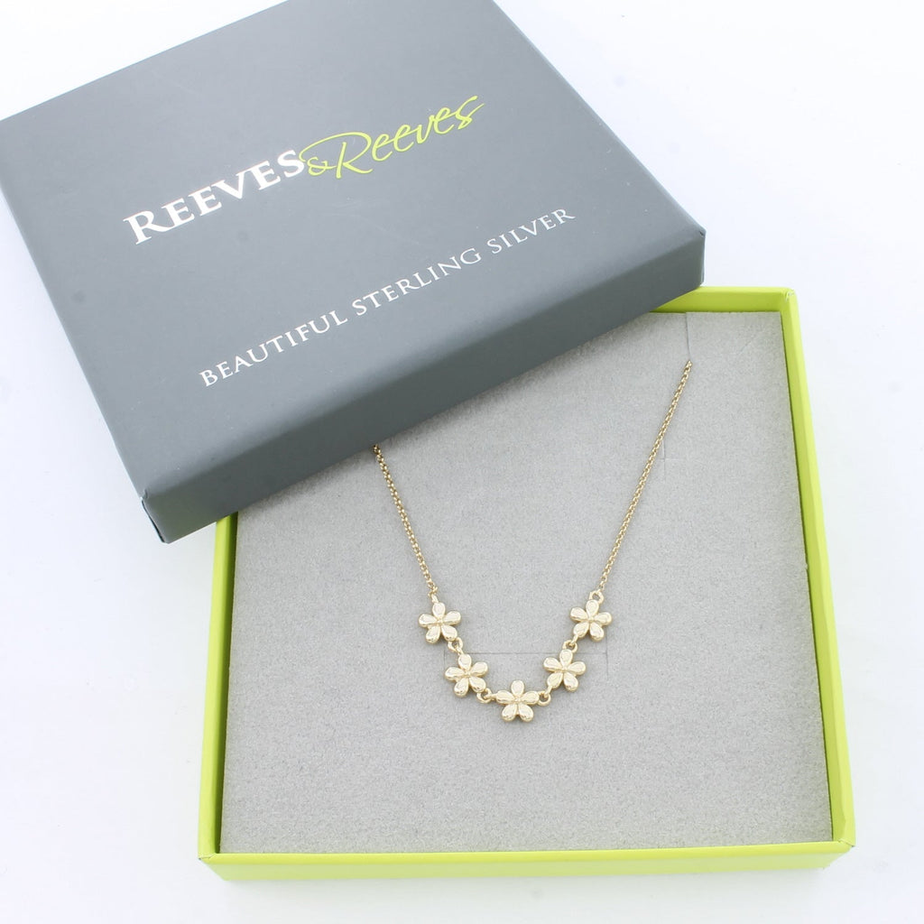 Gold flower necklace with five adjoining flowers at the centre of a gold plated chain. Shown in a Reeves & Reeves branded box which is grey and green.