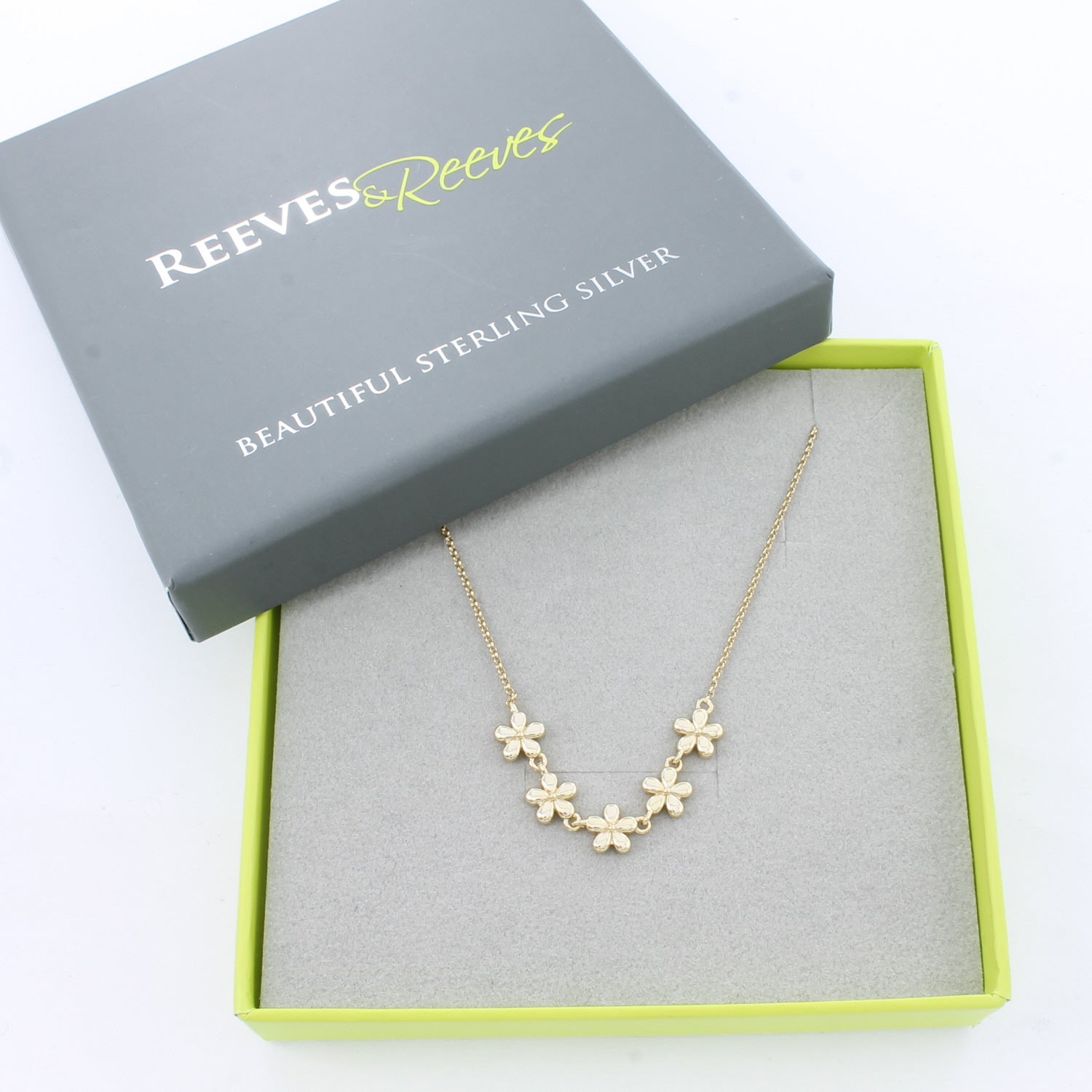 Gold flower necklace with five adjoining flowers at the centre of a gold plated chain. Shown in a Reeves & Reeves branded box which is grey and green.