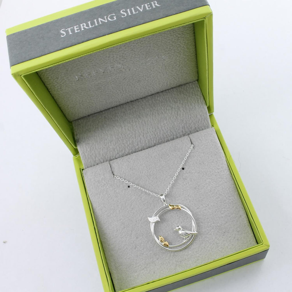 Sterling Silver circular pendant with birds perched on the edges and leaves with gold plate finish. Hanging on a silver adjustable chain and shown in a Reeves & Reeves branded box.