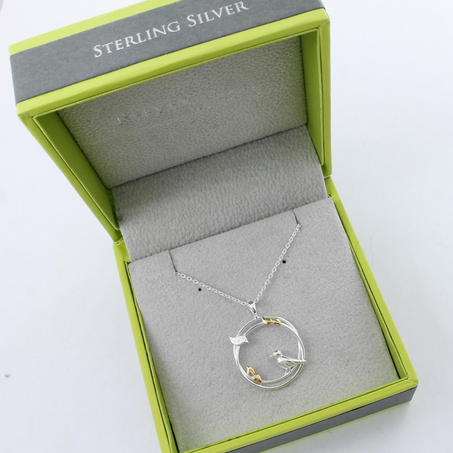 Sterling Silver circular pendant with birds perched on the edges and leaves with gold plate finish. Hanging on a silver adjustable chain and shown in a Reeves & Reeves branded box.
