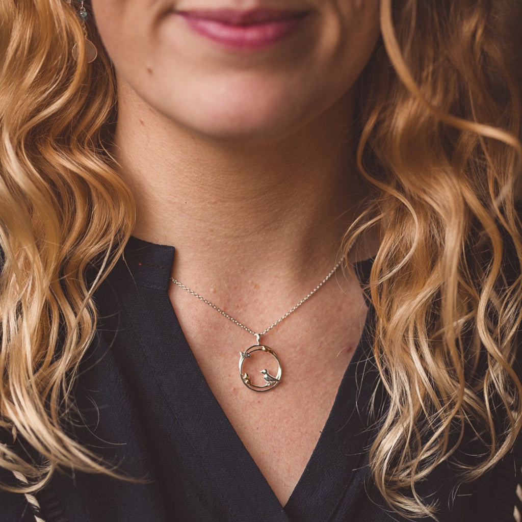 Sterling Silver circular pendant with birds perched on the edges and leaves with gold plated detail, hung on a silver chain and worn on a model.