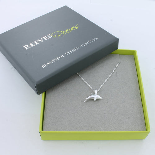 A sterling silver dolphin pendant hanging on a fine silver chain and shown in a Reeves & Reeves grey and green branded gift box.