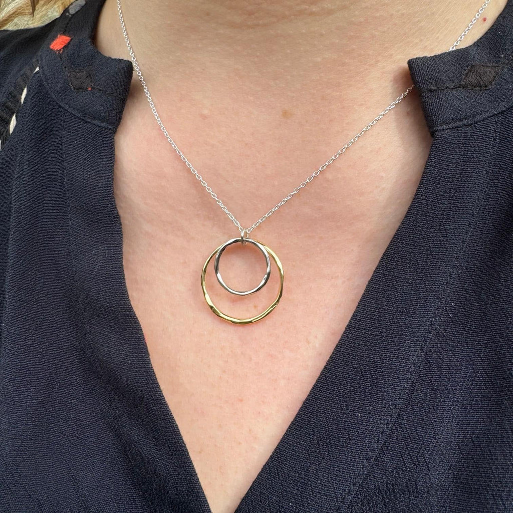A gold plated circular pendant with a smaller silver circular pendant sat inside and hung centrally on a silver adjustable chain.