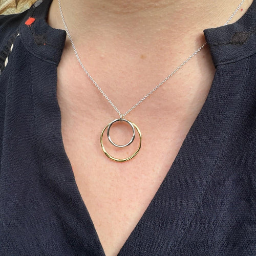 A gold plated circular pendant with a smaller silver circular pendant sat inside and hung centrally on a silver adjustable chain.