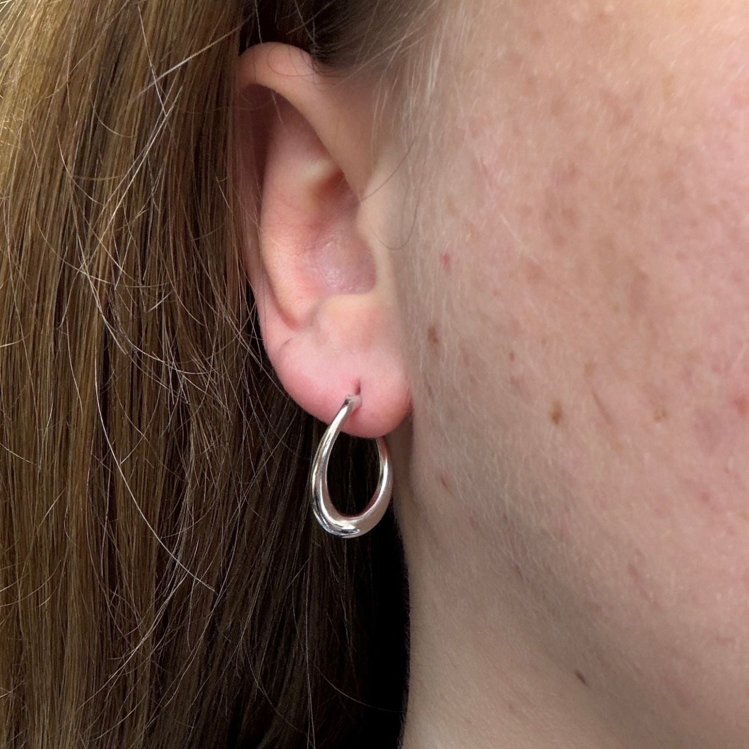 A silver twisted hoop worn in a ladies ear.
