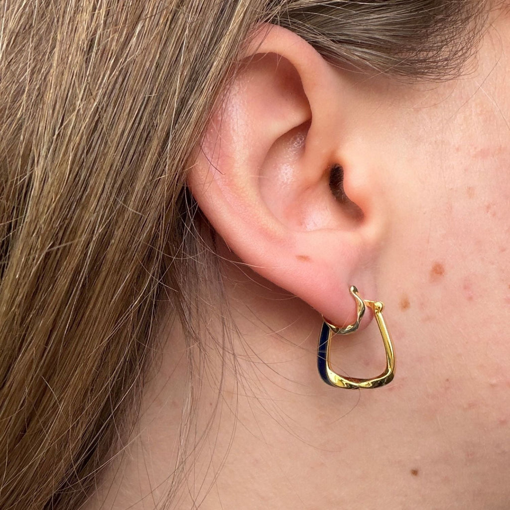 Gold plated square shaped hoop earring with blue enamel detail on one side and a twist at the bottom of the hoop. Worn in a ladies ear.