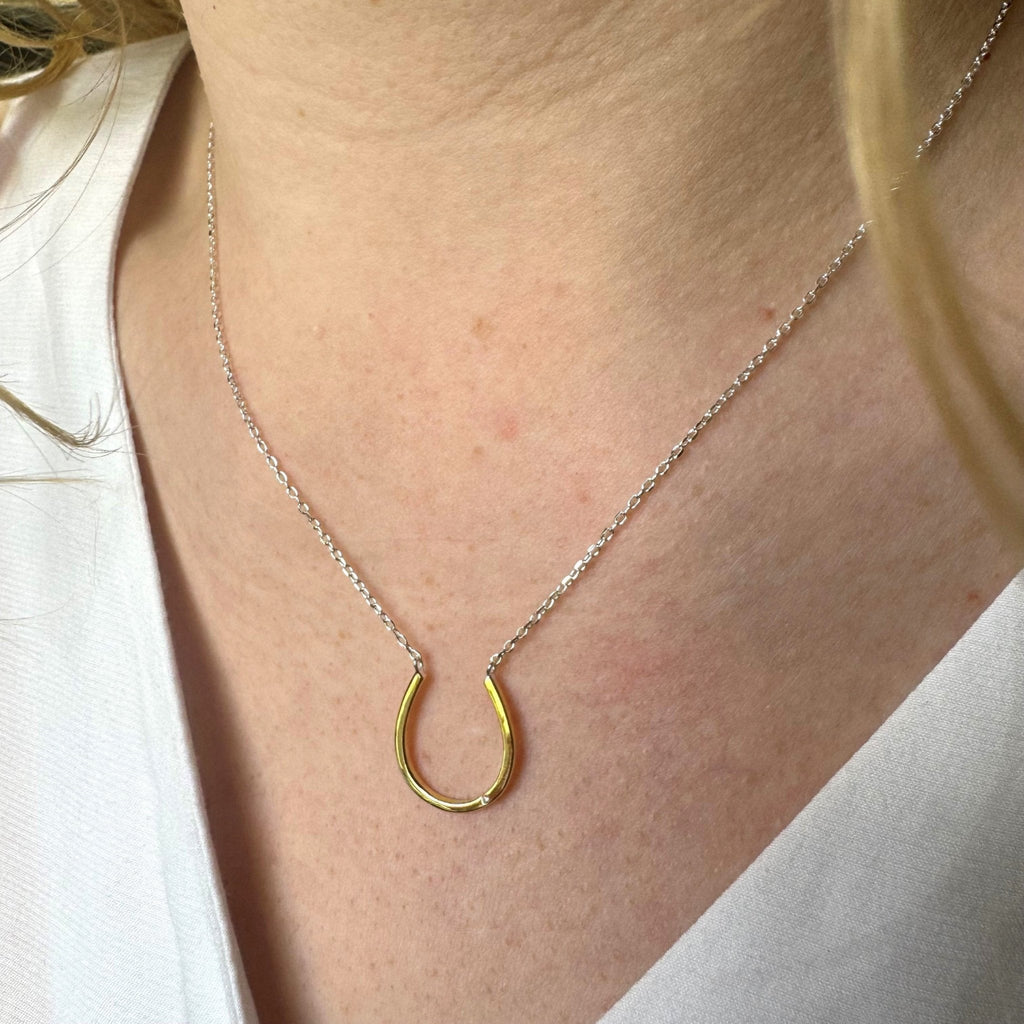 A gold plated horseshoe necklace with a cubic zirconia stone, hung centrally on a fine silver adjustable chain.